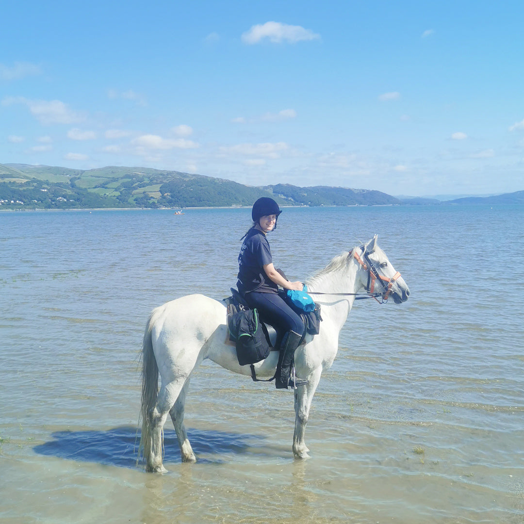 Load image into Gallery viewer, Rider poses in the sea with her horse wearing Freerein equipment expedition saddle bags
